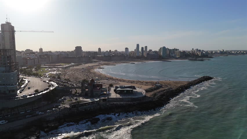 Drone flight over Playa Bristol in Mar del Plata, Argentina, on a crowded day, capturing the vibrant beach scene with many people enjoying the sun.