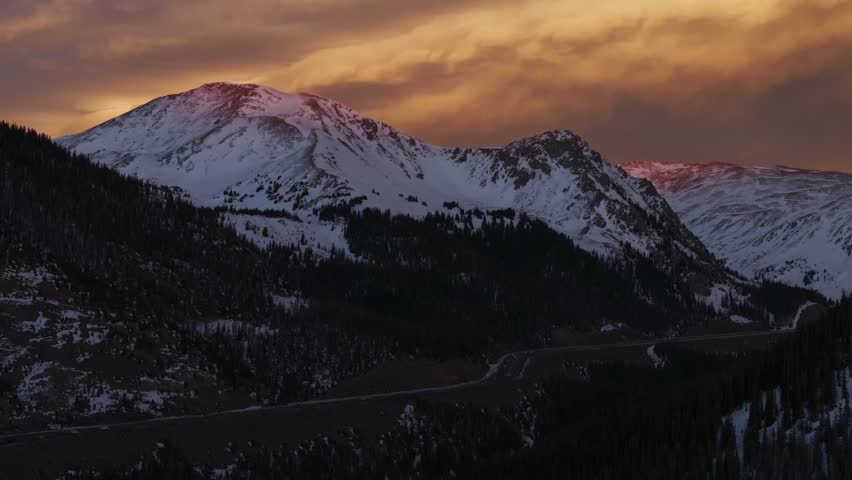 Rocky Mountains Winter solstice Colorado vibrant orange cloudy skies setting sunset aerial drone i70 highway cars trucks traffic Coon Hill Parshall Eisenhower tunnel Continental Divide forward upwards
