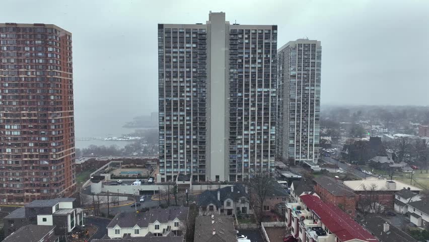 Housing area and high apartment block in Fort Lee, New Jersey during winter. Snowfall and snowstorm in American town. Aerial approaching shot.