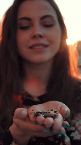 Beautiful girl blowing confetti in the street on sunset. Super slow motion shot. Vertical shot.