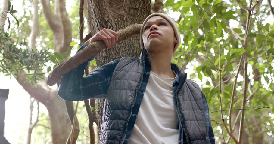 Young man enjoying nature, leaning against tree in peaceful forest setting. relaxation, solitude, tranquility, calm, serenity, greenery