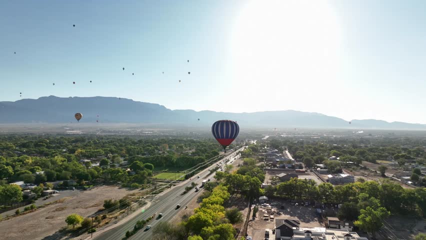 Drone POV of hot air balloons flying over Albuquerque, New Mexico highway near the Sandia Mountains.