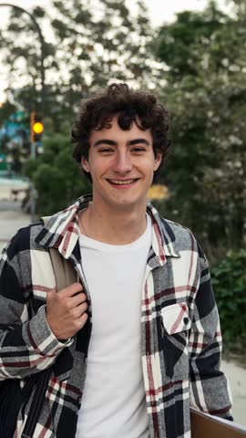 Young hispanic teenager student walking around college campus, smiling at camera 