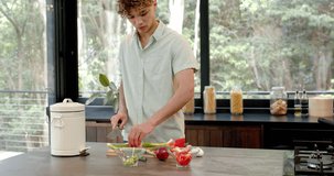 Young man chopping vegetables in modern kitchen with compost bin nearby. Cooking, lifestyle, culinary, sustainability, preparation, healthy eating - Powered by Shutterstock - Get 15% off with code: PIKWIZARD15