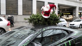 A festive car decorated with a Santa Claus figure and pine branches on its roof parked in a city street. The creative holiday decoration adds a cheerful vibe to the urban environment. - Powered by Shutterstock - Get 15% off with code: PIKWIZARD15