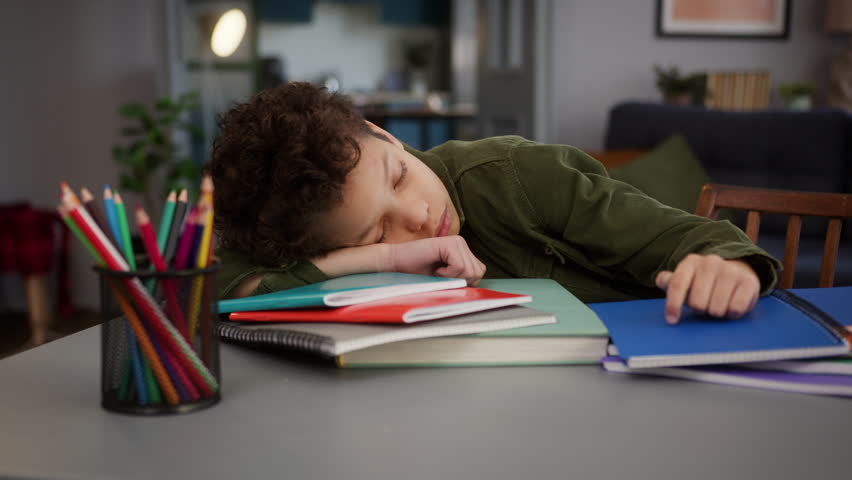Little tired exhausted ill sick insomnia problem African American boy son child kid at home table sleeping napping sleep lying on books studying fatigue pediatric tiredness medicine boring homework