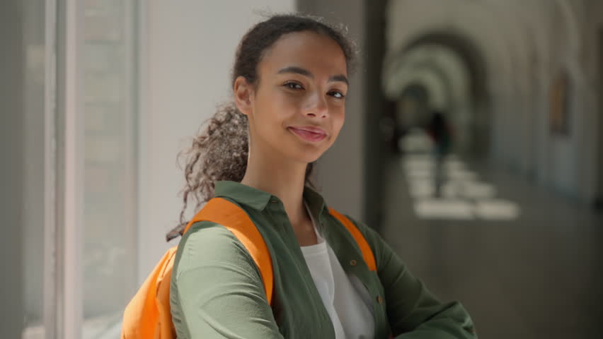 Smiling carefree African American ethnic woman girl student lady pupil female studying learning study learn education in high school university college academy corridor hall looking at camera smile