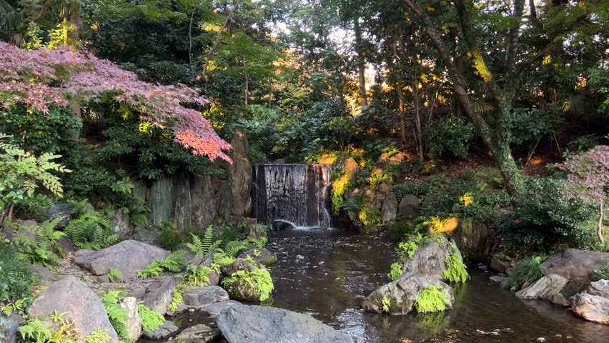 Slow slider over small waterfall in Japanese landscape garden during fall