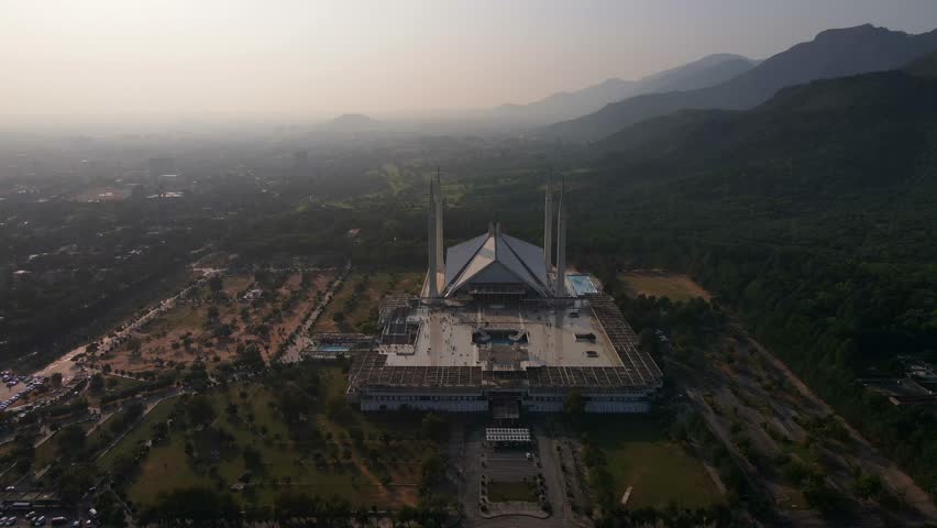 Aerial view of shah faisal mosque surrounded by majestic mountains and lush greenery, islamabad, pakistan.