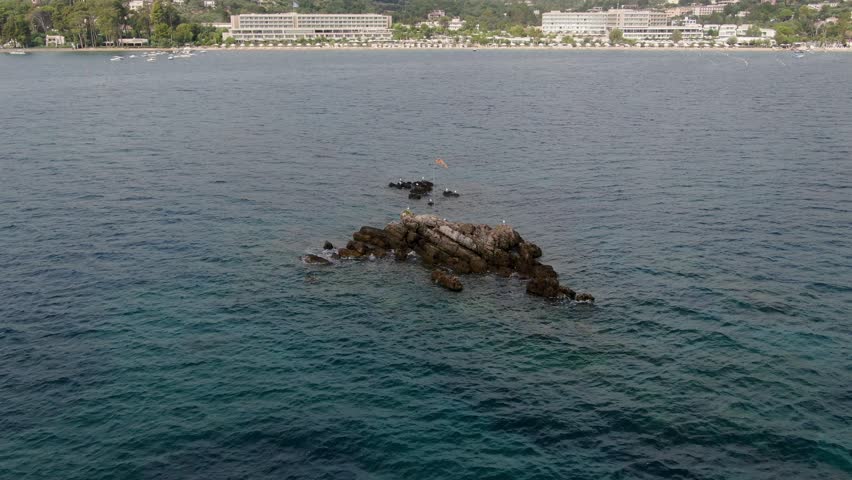 aerial droen video of Rocky island with orange flag in tranquil blue water ,Corfu,Greece