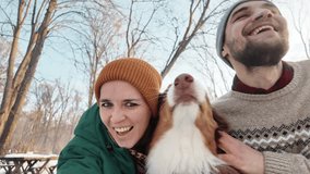 Young couple with Australian shepherd taking selfie on smartphone in snowy winter park, front view. Girl and guy vlogging with dog using camera. Concept of owner and pet having fun outside - Powered by Shutterstock - Get 15% off with code: PIKWIZARD15