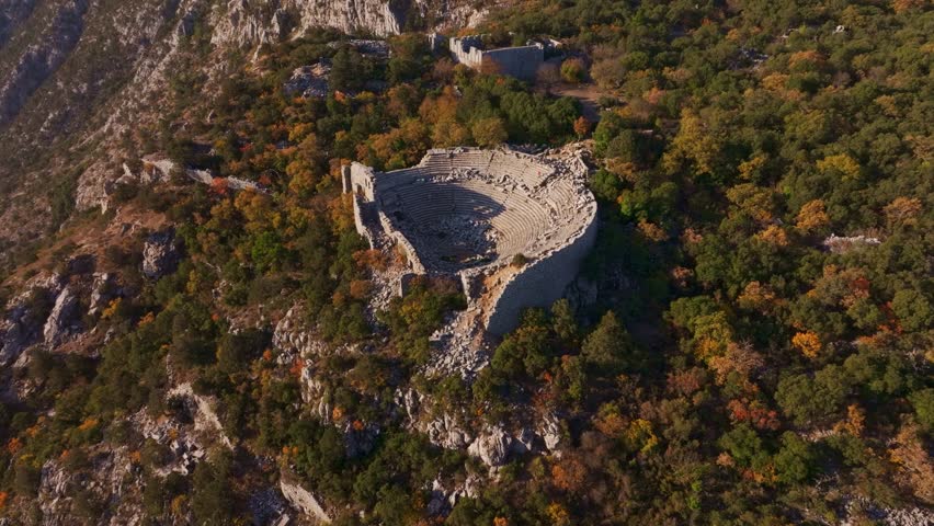 Aerial view of ancient theatre ruins surrounded by autumn forest and rocky mountains, Termessos, Turkey.