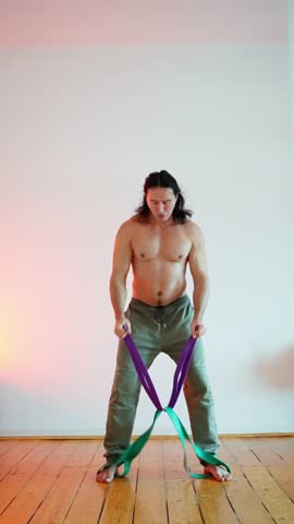 Home training concept where likable concentred sporty man in sportswear doing exercises with rubber resistance strap on the floor at home in the evening