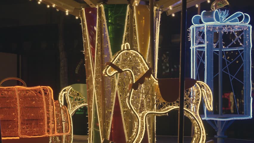 Details of a festive merry-go-round carousel in close-up. The carousel, decorated with garlands, spins at night without people.