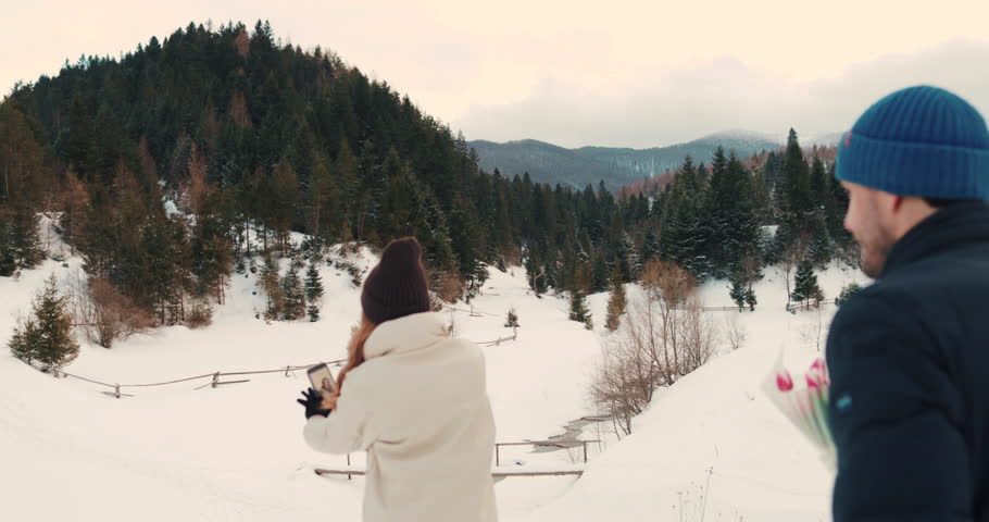 Romantic winter scene with a young couple in love. The man surprises his partner with a bouquet of flowers and a cozy date outdoors amidst a snowy landscape. Love and joy fill the air.