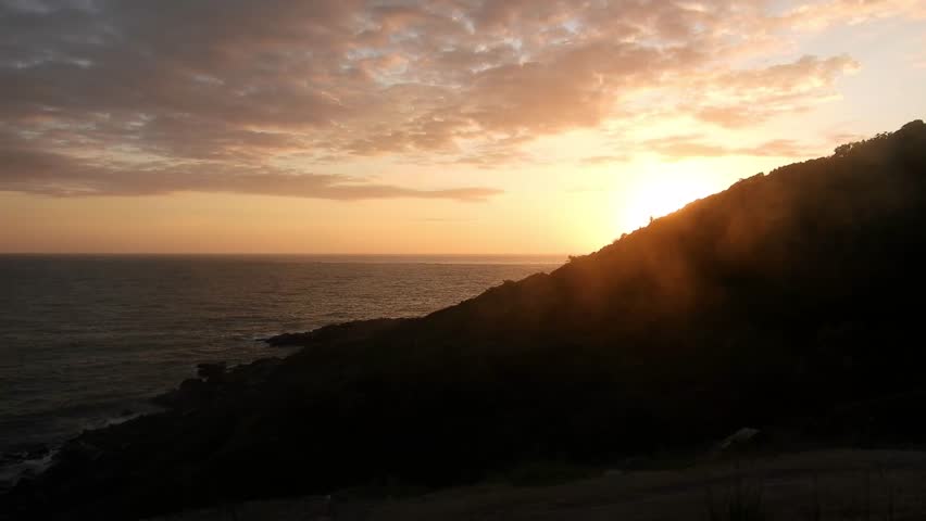 Sunrise over the sea with a silhouetted tropical mountain on the right