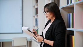 Mature businesswoman writing on clipboard, inside office with book shelves - Powered by Shutterstock - Get 15% off with code: PIKWIZARD15