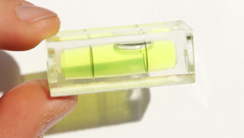 Hand holding a transparent level tool with liquid bubble for measurement accuracy in bright light.