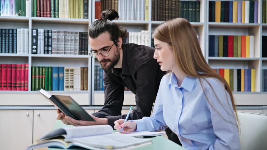 Teenage student girl studying with male teacher inside classroom library