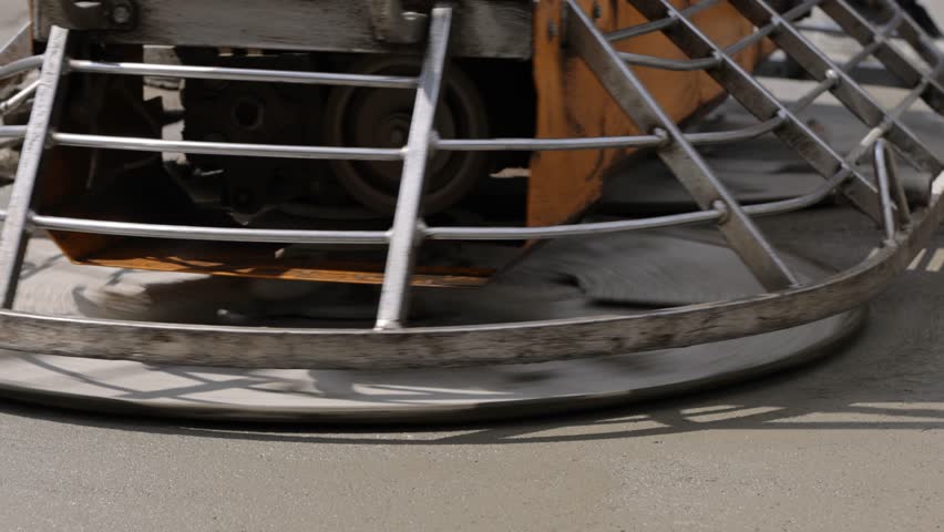 Construction worker leveling concrete surface with power trowel machine