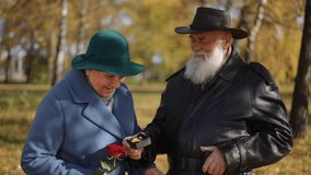 An elderly man presenting an engagement ring in a small box to a smiling woman holding a red rose. The touching moment takes place in a serene autumn park, symbolizing love, commitment, and a timeless - Powered by Shutterstock - Get 15% off with code: PIKWIZARD15
