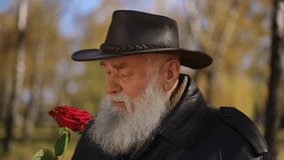 A humorous moment captured as an elderly man sneezes while smelling a vibrant red rose in a serene autumn park. Dressed in a leather coat and hat, his expression adds character and warmth to the - Powered by Shutterstock - Get 15% off with code: PIKWIZARD15