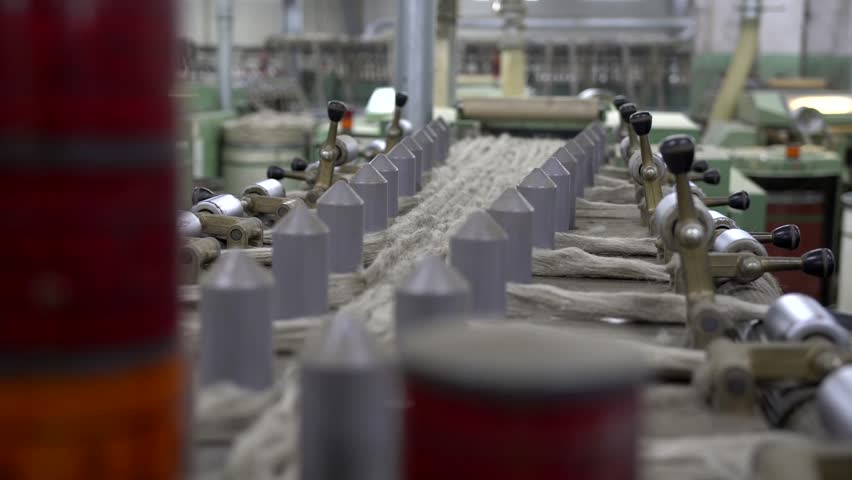 Detailed view of flax fibers being stretched and aligned on a spinning machine in a factory, highlighting the intricate process of textile production and sustainable material handling.