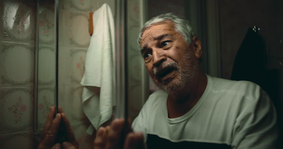 Elderly man raising his hands to the mirror, pleading silently for answers as he faces the pain of his past and wrestles with overwhelming guilt in an emotional scene