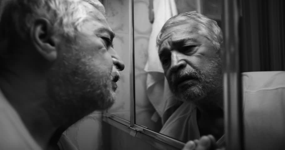 Elderly man confronting his reflection in a bathroom mirror, eyes filled with anguish, as he struggles with regret, isolation, and the weight of his emotions in a raw moment
