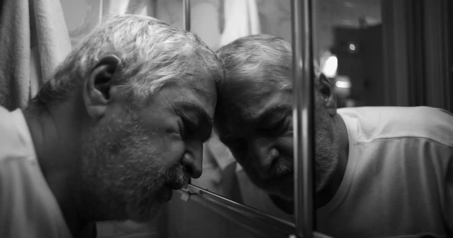 Elderly man pressing his forehead against a bathroom mirror, overwhelmed by sorrow and the weight of his emotions, in a profoundly raw and introspective moment, black and white