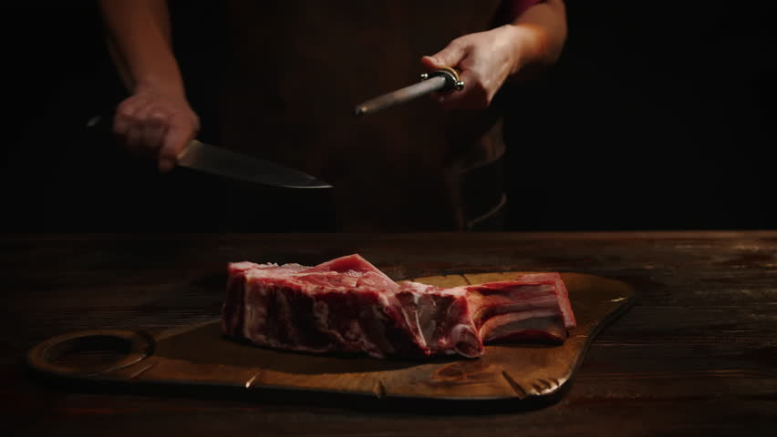 Butcher sharpening knife in front of cutting table. Butchering raw meat in butcher's shop