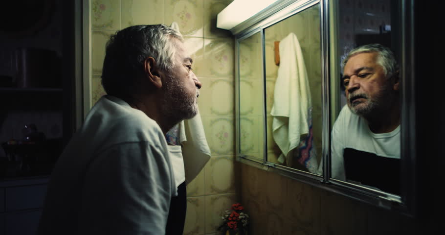 Elderly man leaning into his reflection in a bathroom mirror, eyes filled with intensity, as if searching for lost time and grappling with his own existence