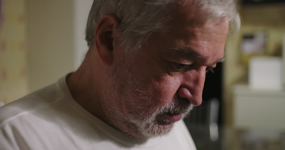 Close-up of an elderly man with dementia or age-related illness in a kitchen, looking down in deep thought, emphasizing aging, health, and introspection