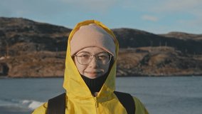 A tourist stands in windy weather, wearing a waterproof raincoat, next to the cold coast, squinting from the bright northern sun. Portrait. - Powered by Shutterstock - Get 15% off with code: PIKWIZARD15