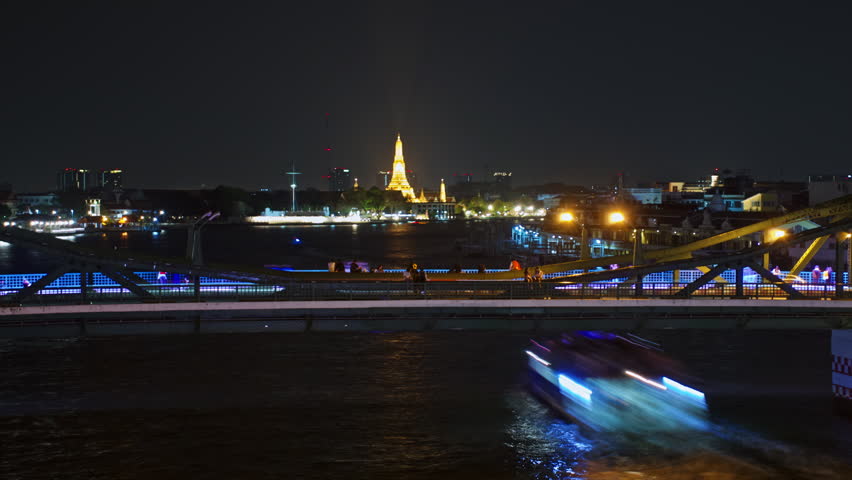 Stunning night view of a vibrant cityscape featuring a well-lit bridge crossing over water. The scene captures a temple illuminated in the background, surrounded by urban lights and reflections on the