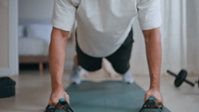 Young sportsman performing pushups with handles at home fitness session closeup. Motivated man practicing strength training with effort. Determined hispanic athlete having active workout in apartment. - Powered by Shutterstock - Get 15% off with code: PIKWIZARD15