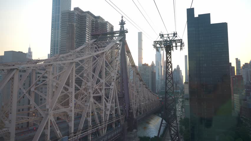 This image showcases the Queensboro Bridge against the backdrop of New York City's skyline during sunset. The golden sunlight highlights the bridge's intricate steel structure and towering skyscrapers
