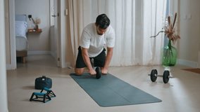 Man training abs roller at home workout. Focused hispanic athlete strengthening abdominal muscles practicing sport exercises on mat. Active fit sportsman exercising with gymnastic wheel in apartment. - Powered by Shutterstock - Get 15% off with code: PIKWIZARD15