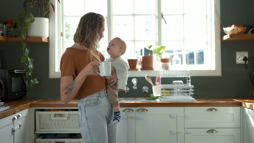 Coffee, kiss or mother dancing with baby in the morning with kid or care drinking beverage in family home. Happy parent, drinking tea or mom enjoying bonding time with newborn child in house kitchen