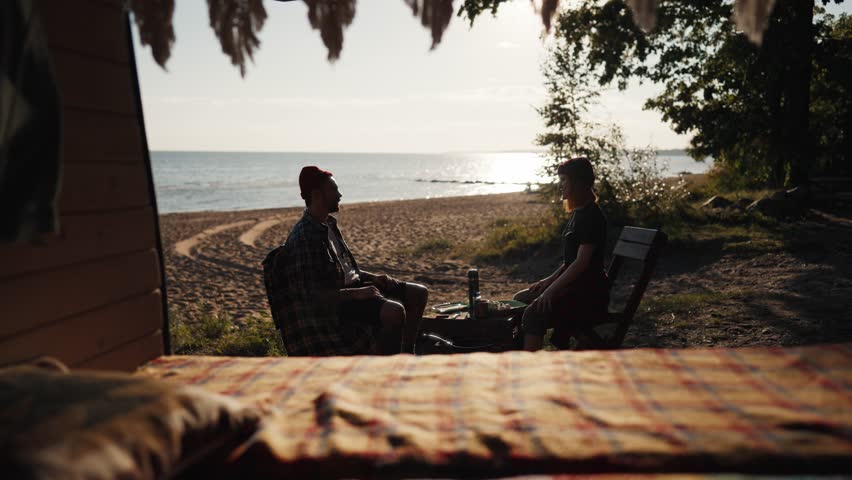 Trip by motorhome, calm breakfast on beach of sea or lake in sunny morning. Two campers relaxing and chatting, enjoying solitude, view from cozy camper car, traveling in nature by auto across country