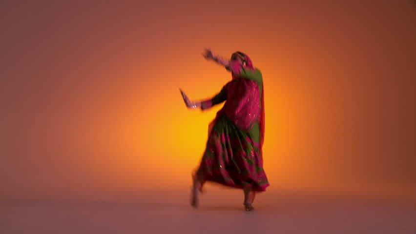 Indian girl in traditional folk costume starts dancing against an orange colored