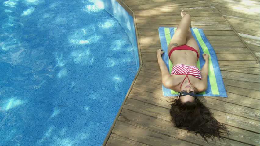 Beautiful woman sunbathing next to a swimming pool.