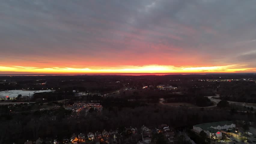 A radiating burst of light exploding through the cracks of an overcast sky just over the horizon as the sun begins to set and the view begins to rise