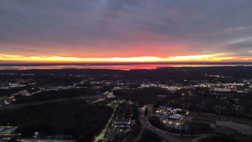 A radiating burst of light exploding through the cracks of an overcast sky just over the horizon as the sun sets while commuters below make the journey to their destination.