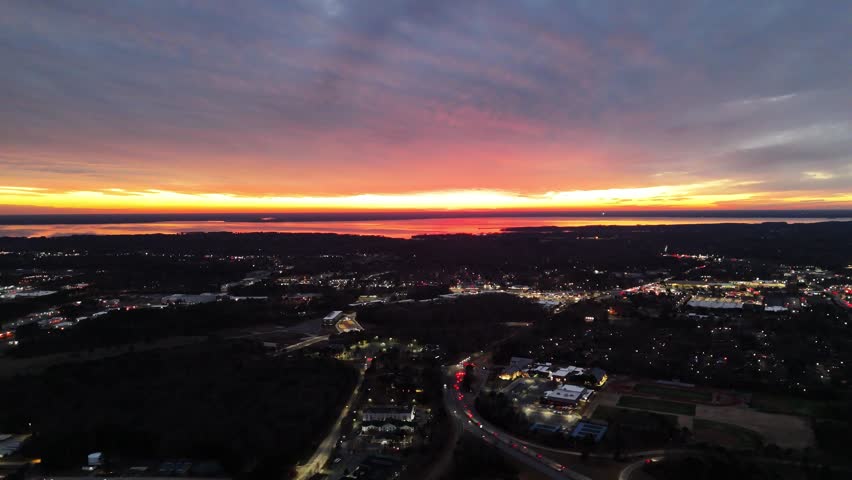 A radiating burst of light exploding through the cracks of an overcast sky just over the horizon as the sun sets while commuters below make the journey to their destination.