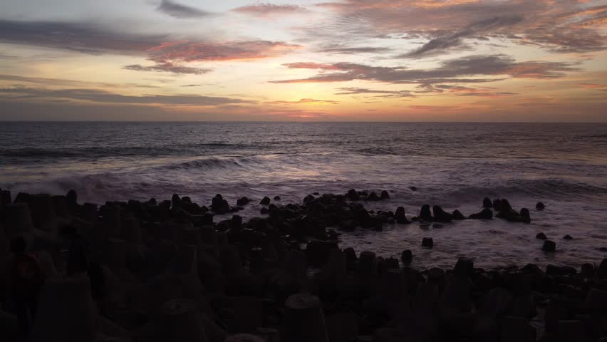 Sunset over the beach, big waves crashing on concrete or Tetrapod. Golden hour on the horizon. sunset 4k. Sunrise in the Indian Ocean. Glagah Beach, Yogyakarta.