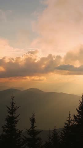 Vertical screen Golden Light Over Smoky Mountains, USA tranquil scene of Smoky Mountains during sunset, with rays of golden light breaking through clouds highlighting rolling hills tree silhouettes.