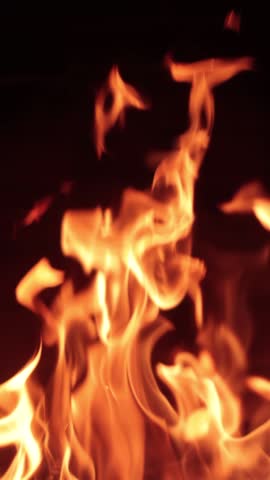 A vertical close-up of orange fire with big flames against dark background