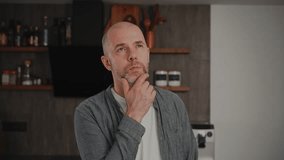 A middle-aged man in casual clothes, standing in his kitchen. He looks deep in thought, contemplating different options and struggling to make a decision. - Powered by Shutterstock - Get 15% off with code: PIKWIZARD15
