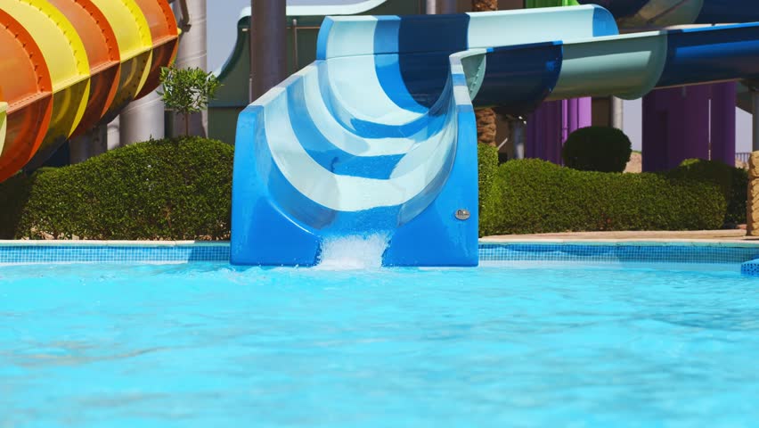 A teenage girl slides down a slide in a water park on a large inflatable ring.
